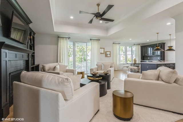 living room featuring ceiling fan, recessed lighting, a fireplace, light wood-type flooring, and a tray ceiling