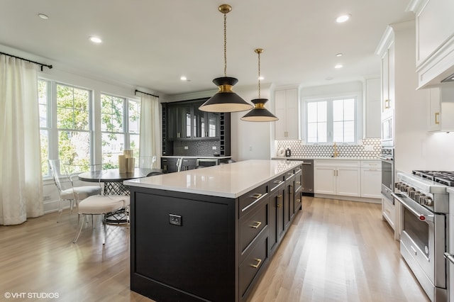 kitchen featuring hanging light fixtures, light wood-type flooring, decorative backsplash, a kitchen island, and stainless steel appliances