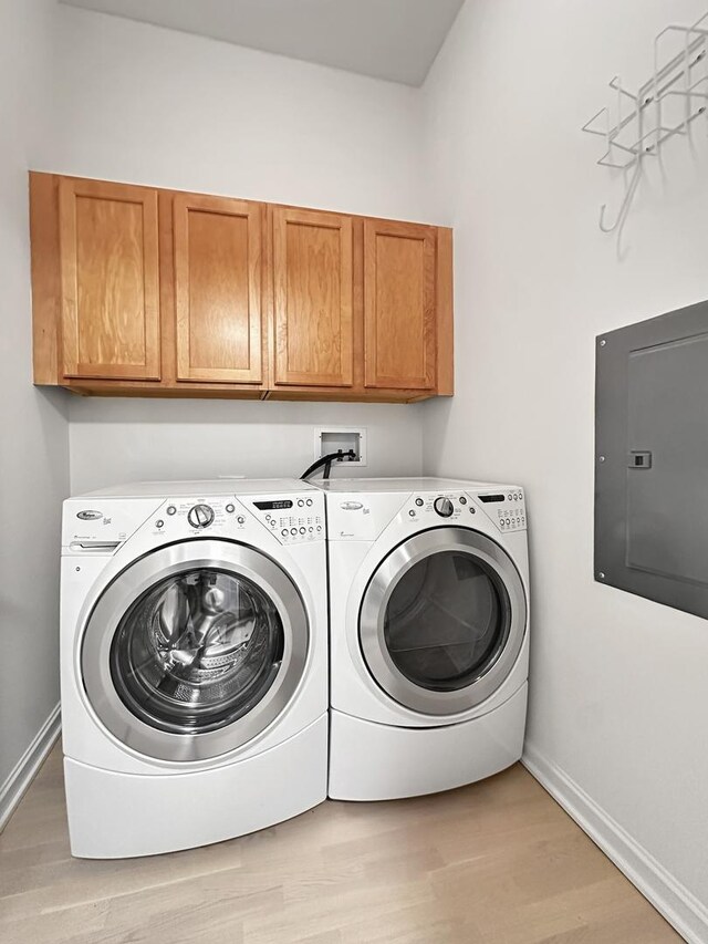 laundry area with light wood-type flooring, cabinets, electric panel, and washer and clothes dryer