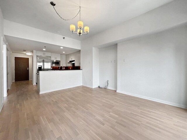 unfurnished living room featuring sink, light hardwood / wood-style floors, and a chandelier