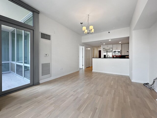 unfurnished living room featuring a wealth of natural light, a notable chandelier, sink, and light wood-type flooring