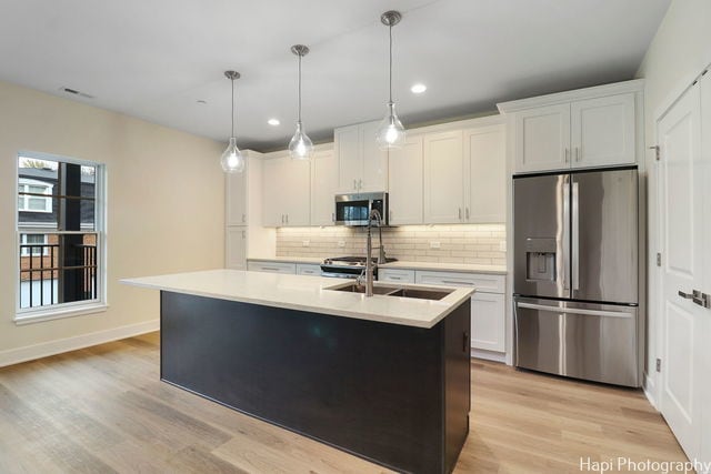 kitchen with pendant lighting, white cabinetry, stainless steel appliances, and an island with sink