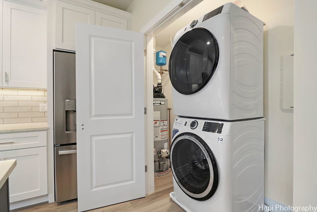 laundry room with stacked washer / dryer, light hardwood / wood-style flooring, and gas water heater