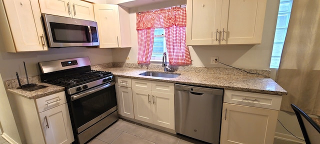 kitchen with white cabinets, light tile floors, stainless steel appliances, light stone countertops, and sink