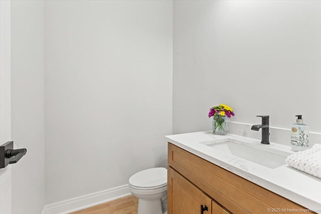 half bathroom featuring baseboards, toilet, vanity, and wood finished floors