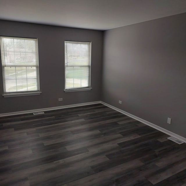 empty room with dark hardwood / wood-style flooring and plenty of natural light