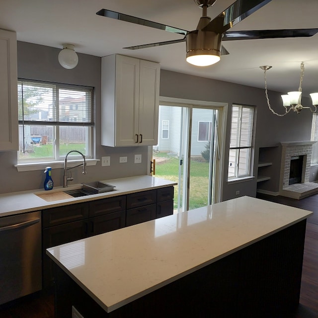 kitchen with white cabinets, stainless steel dishwasher, a notable chandelier, a fireplace, and sink