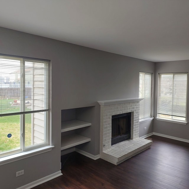 unfurnished living room with dark wood-type flooring and a brick fireplace