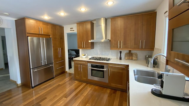 kitchen featuring wood finished floors, a sink, appliances with stainless steel finishes, wall chimney exhaust hood, and backsplash