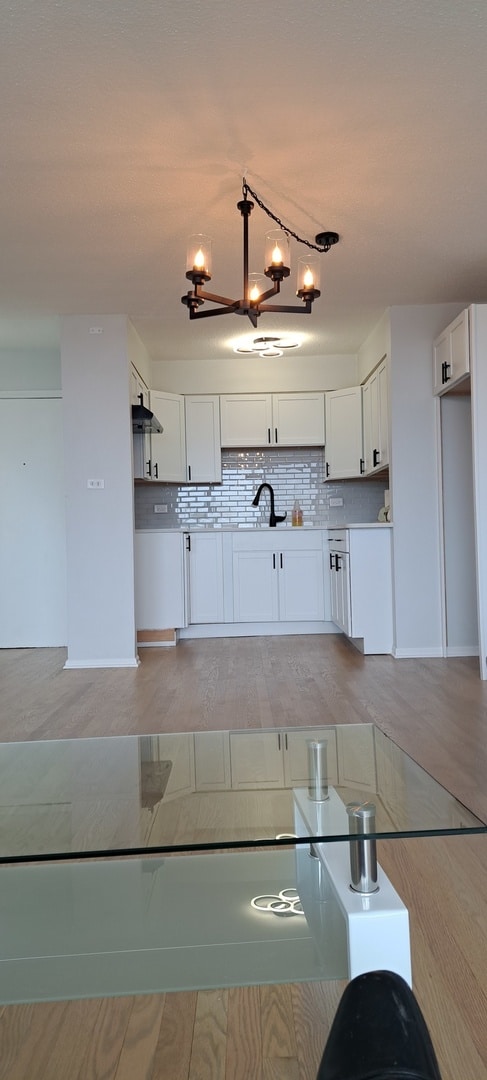 kitchen featuring a notable chandelier, white cabinets, light hardwood / wood-style floors, and tasteful backsplash