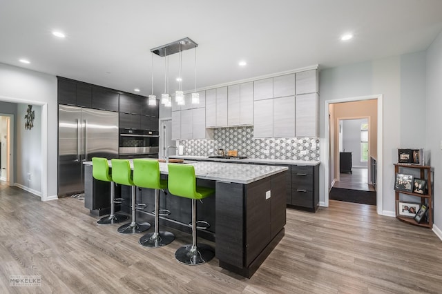 kitchen with pendant lighting, a kitchen bar, stainless steel appliances, an island with sink, and light wood-type flooring