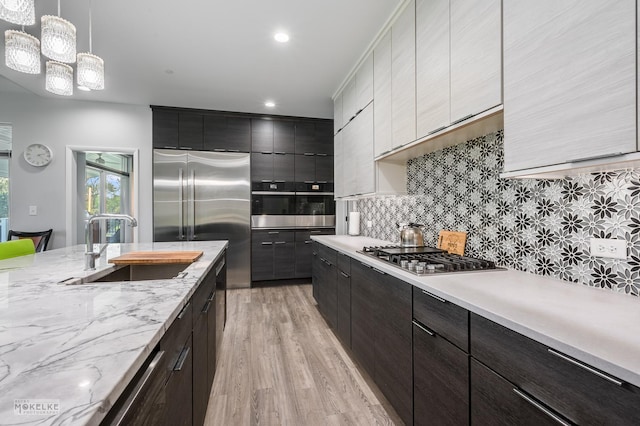 kitchen with stainless steel appliances, decorative light fixtures, white cabinets, light hardwood / wood-style flooring, and sink