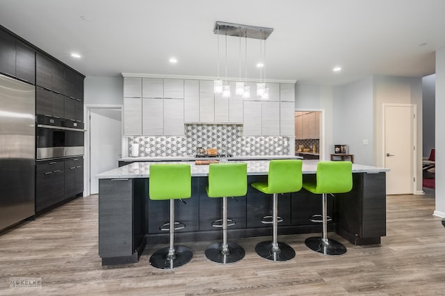 kitchen with pendant lighting, appliances with stainless steel finishes, a kitchen island with sink, and a breakfast bar area