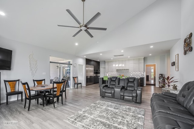 living room with high vaulted ceiling, ceiling fan, and light hardwood / wood-style flooring