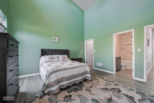 bedroom featuring high vaulted ceiling, connected bathroom, and hardwood / wood-style floors