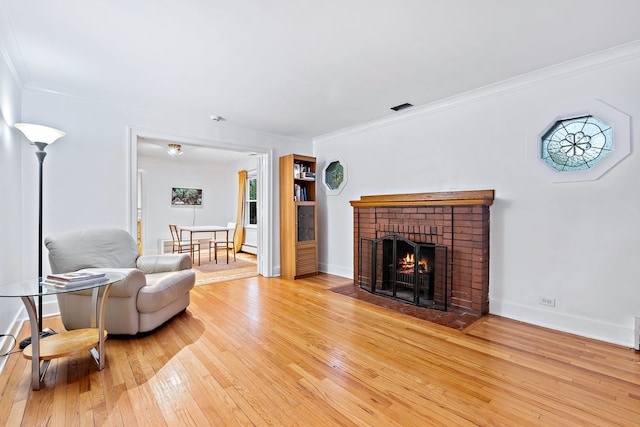 living room with light wood-type flooring, ornamental molding, and a brick fireplace