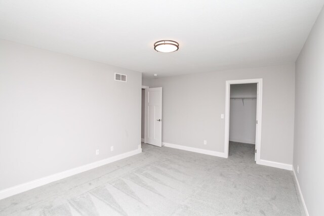 unfurnished bedroom with a walk in closet, a closet, and light carpet