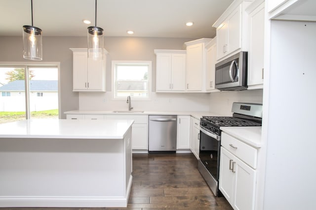 kitchen with stainless steel appliances, sink, white cabinets, dark wood-type flooring, and hanging light fixtures