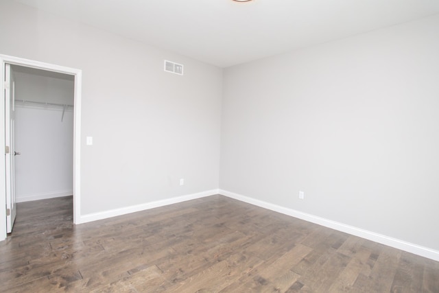 unfurnished bedroom featuring a walk in closet, dark wood-type flooring, and a closet