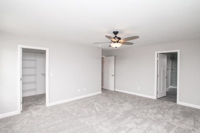 unfurnished bedroom with a walk in closet, ceiling fan, and light carpet