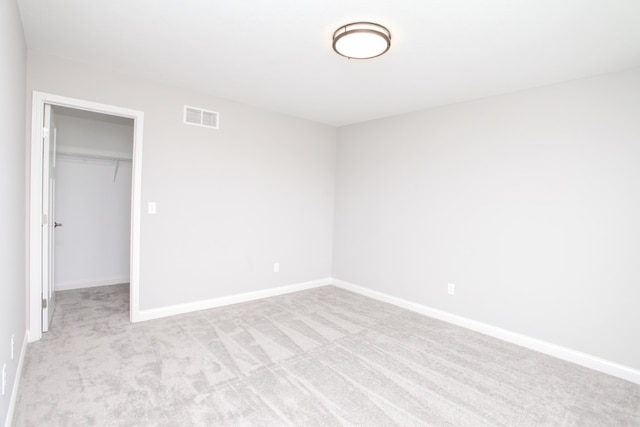 unfurnished bedroom featuring a walk in closet, light colored carpet, and a closet