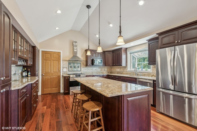 kitchen with lofted ceiling, a kitchen island, dark wood-type flooring, wall chimney range hood, and appliances with stainless steel finishes