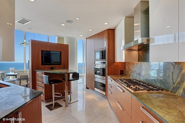 kitchen featuring a kitchen breakfast bar, a water view, stainless steel appliances, tasteful backsplash, and wall chimney exhaust hood