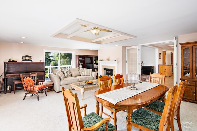 dining area with ceiling fan, a tiled fireplace, light carpet, and a raised ceiling