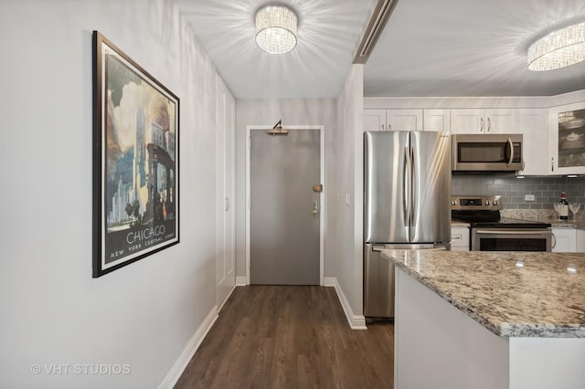 kitchen featuring white cabinets, decorative backsplash, glass insert cabinets, light stone counters, and stainless steel appliances