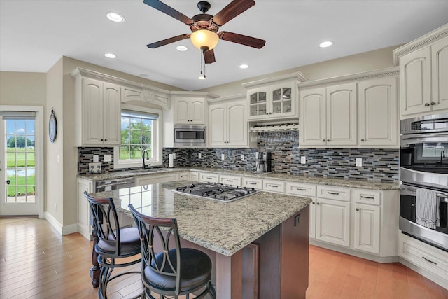 3001 E Stone Creek Blvd, Urbana, IL 61802 - kitchen with appliances with stainless steel finishes, a kitchen bar, ceiling fan, light wood-type flooring, and backsplash