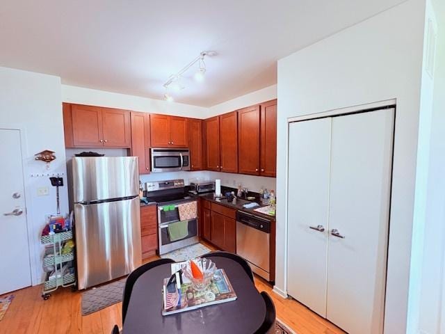 kitchen featuring appliances with stainless steel finishes, light wood-style flooring, dark countertops, and brown cabinets