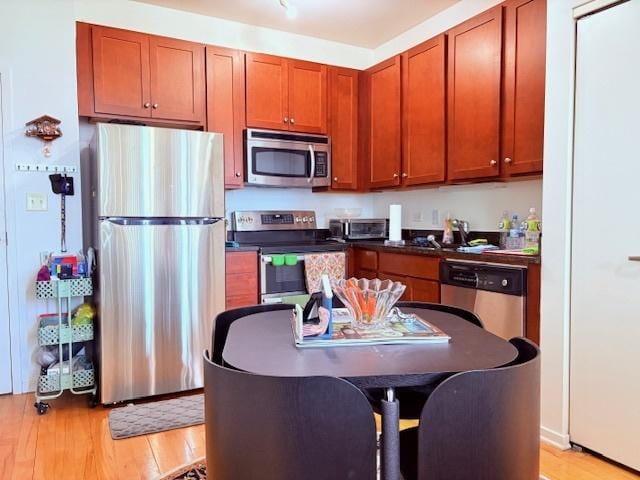 kitchen with appliances with stainless steel finishes, light wood finished floors, dark countertops, and brown cabinetry