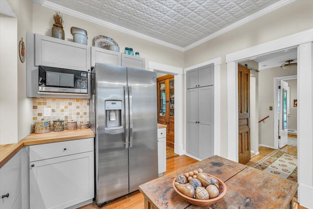 kitchen with appliances with stainless steel finishes, an ornate ceiling, wooden counters, backsplash, and light wood finished floors
