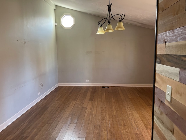 spare room with dark wood-type flooring, a chandelier, and vaulted ceiling