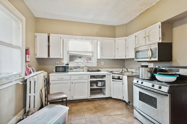 kitchen featuring white stove, sink, radiator, white cabinets, and light tile patterned floors