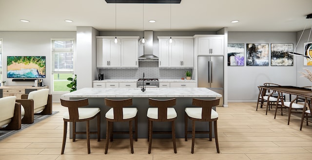 kitchen with stainless steel refrigerator, white cabinetry, wall chimney exhaust hood, light stone counters, and decorative light fixtures