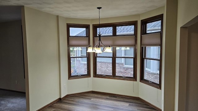 unfurnished dining area featuring baseboards, wood finished floors, and a notable chandelier