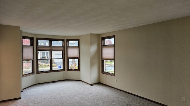 empty room with light carpet, a textured ceiling, visible vents, and baseboards