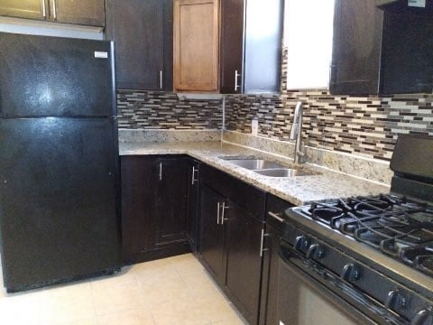 kitchen featuring black fridge, range, backsplash, sink, and light tile floors