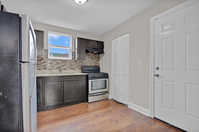 kitchen featuring dark brown cabinetry, backsplash, stainless steel range with gas stovetop, fridge, and light wood-type flooring