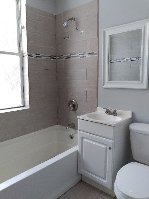 full bathroom with tile floors, tiled shower / bath combo, vanity, and toilet