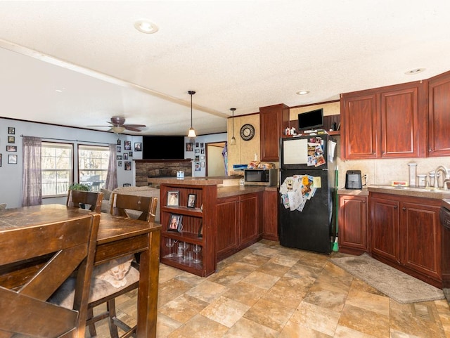 kitchen featuring pendant lighting, ceiling fan, black refrigerator, and a fireplace