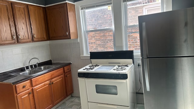 kitchen with light tile patterned flooring, sink, stainless steel refrigerator, decorative backsplash, and white range oven