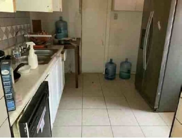 kitchen with stainless steel fridge, white cabinetry, light tile patterned floors, and sink