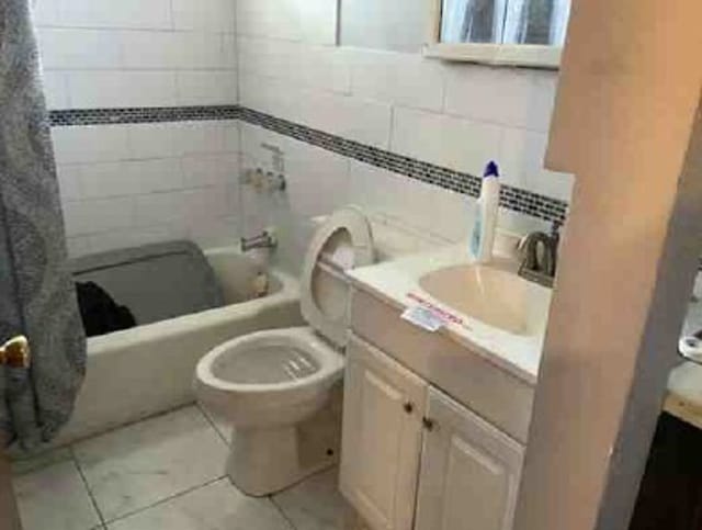 full bathroom featuring shower / tub combo, backsplash, vanity, tile walls, and toilet