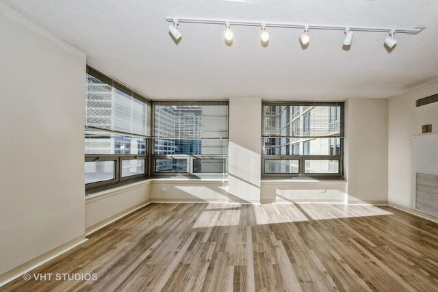 unfurnished room featuring rail lighting, hardwood / wood-style flooring, and a textured ceiling