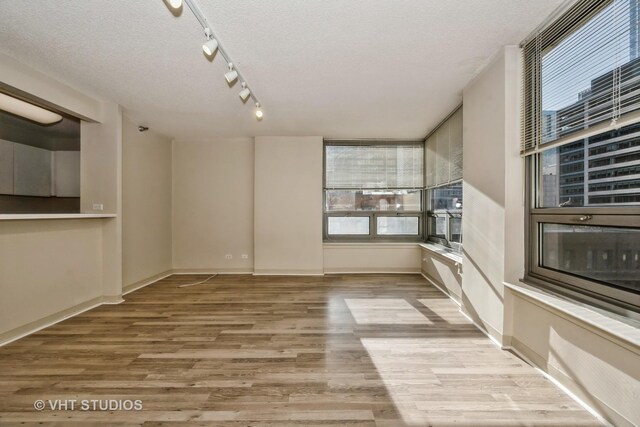 spare room with rail lighting, a textured ceiling, and light hardwood / wood-style floors