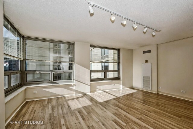 unfurnished room featuring hardwood / wood-style floors, expansive windows, track lighting, and a textured ceiling