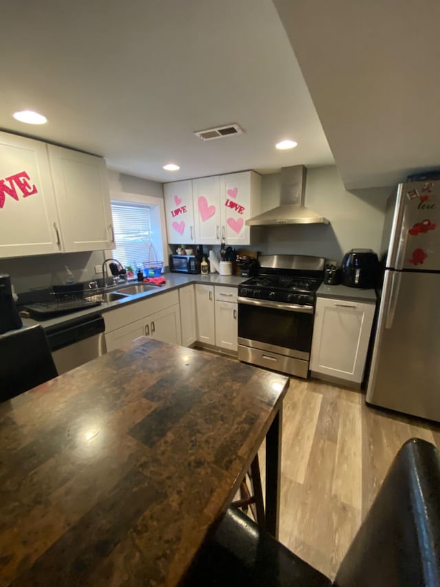 kitchen with appliances with stainless steel finishes, white cabinets, light wood-type flooring, and wall chimney exhaust hood