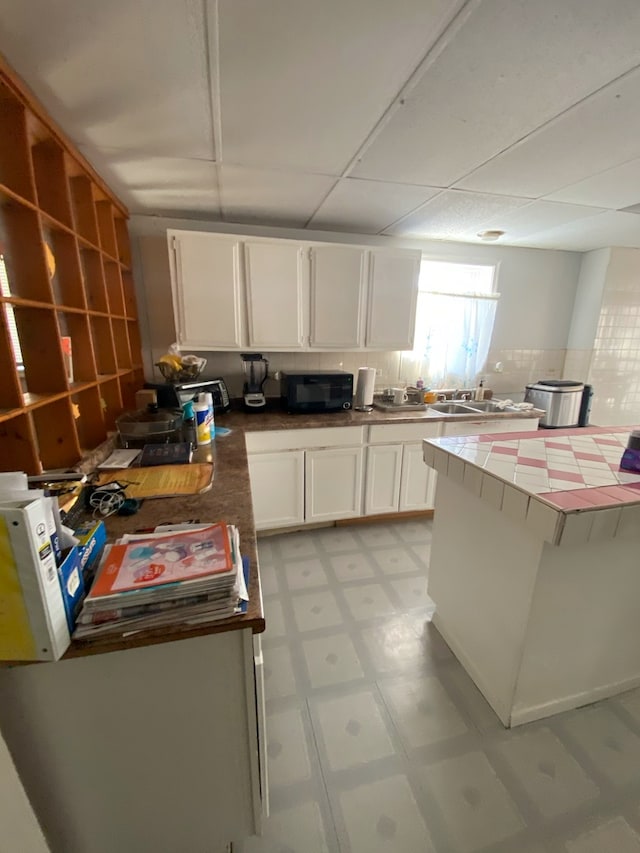 3806 S Wolcott Ave, Chicago, IL 60609 - kitchen featuring tile countertops, a paneled ceiling, white cabinetry, and light tile floors